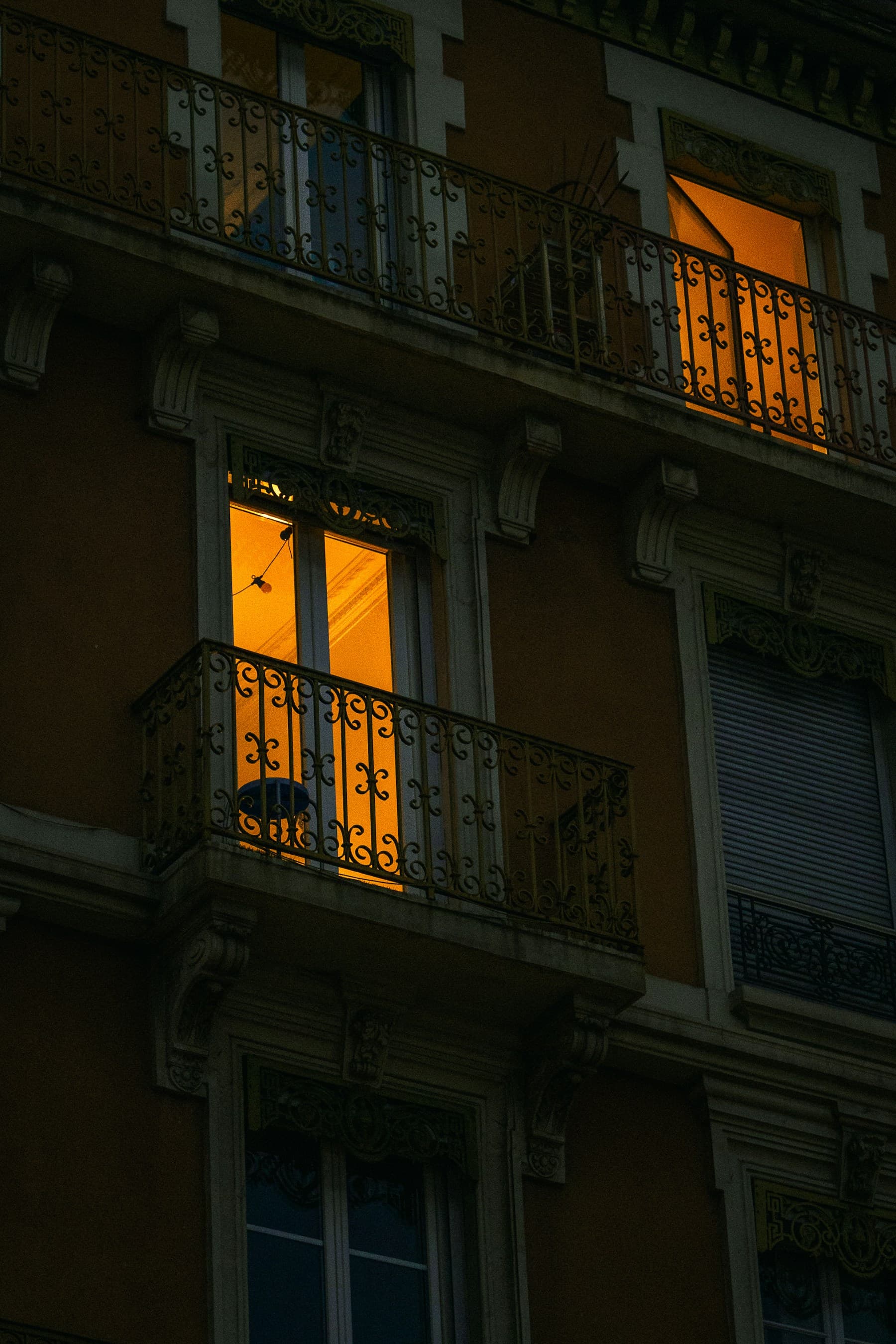 Traditional wrought-iron balcony grill on an old apartment facade — the cage look an invisible grill replaces